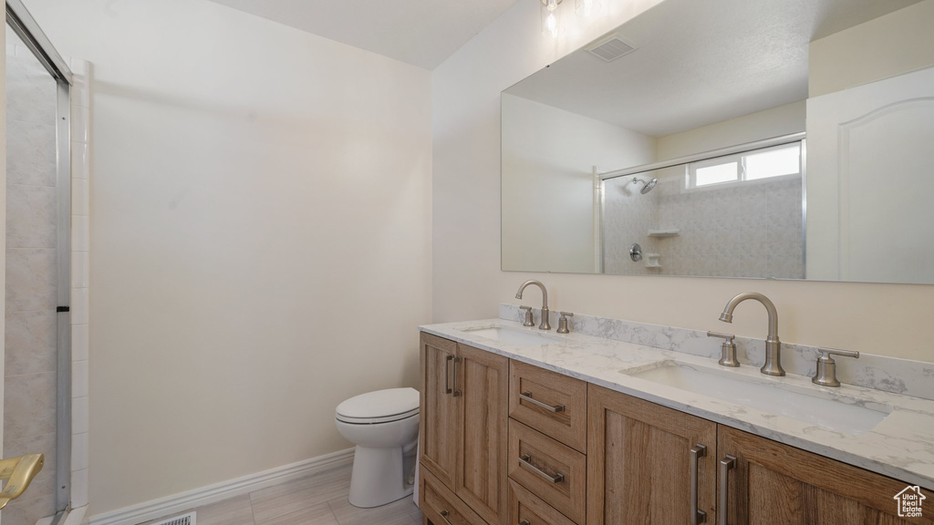 Bathroom with a sink, a shower with door, toilet, and visible vents