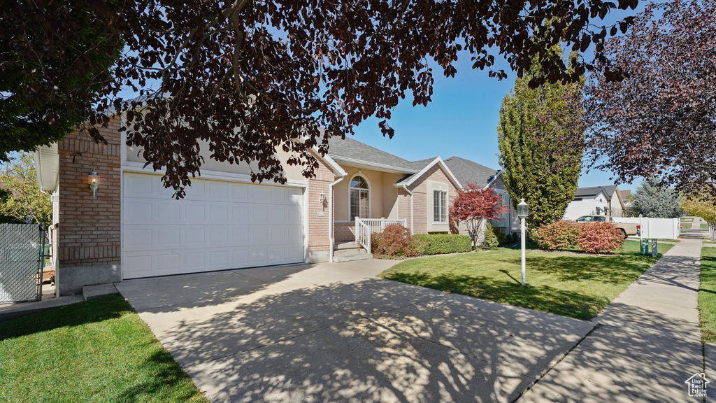 View of front facade with a garage, fence, a front yard, brick siding, and driveway
