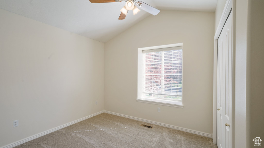 Spare room featuring visible vents, lofted ceiling, light carpet, baseboards, and ceiling fan
