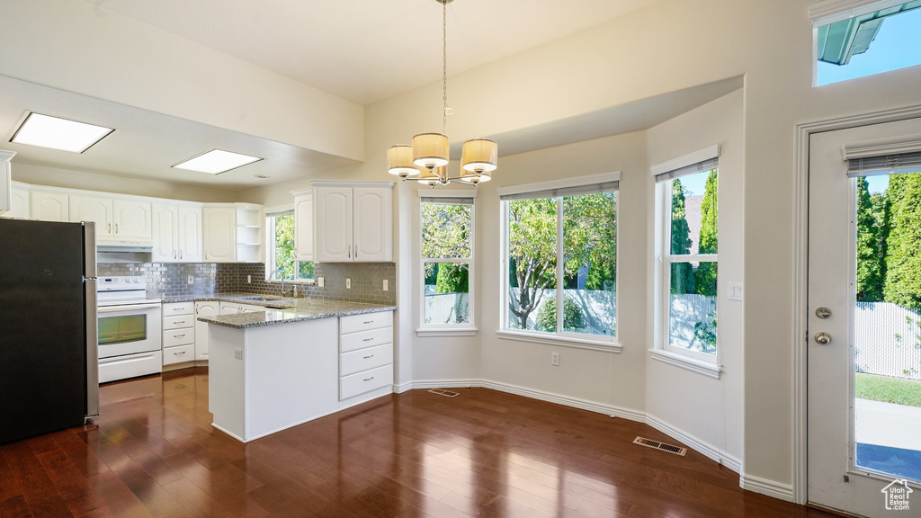 Kitchen with visible vents, freestanding refrigerator, a peninsula, white range with electric stovetop, and white cabinetry
