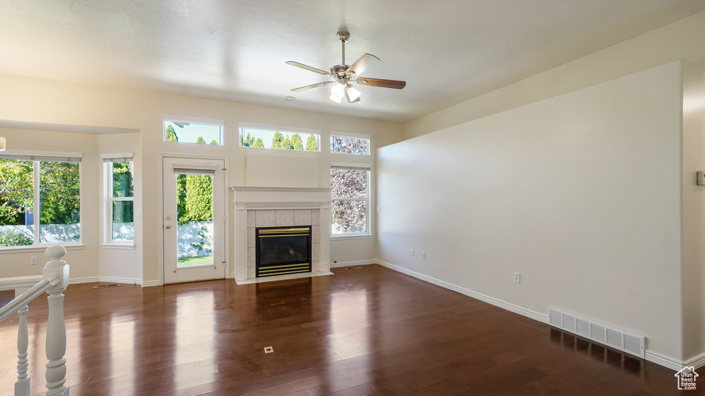 Unfurnished living room featuring ceiling fan, visible vents, a tiled fireplace, wood finished floors, and baseboards