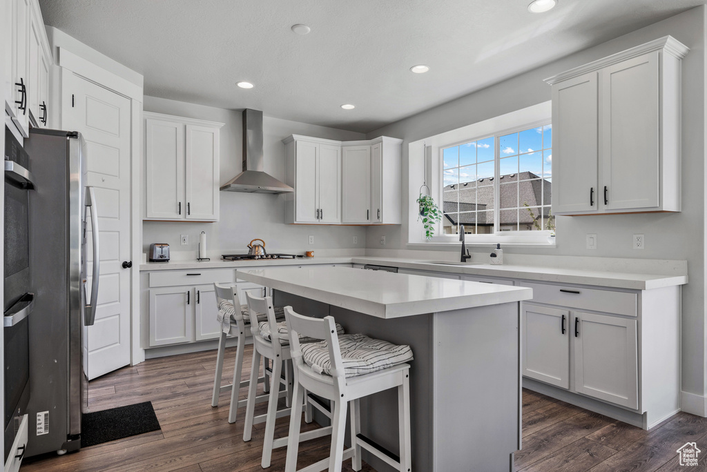 Kitchen featuring a kitchen breakfast bar, wall chimney range hood, dark wood-type flooring, a center island, and a sink