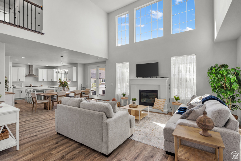 Living room with a high ceiling, an inviting chandelier, dark wood finished floors, a glass covered fireplace, and a healthy amount of sunlight