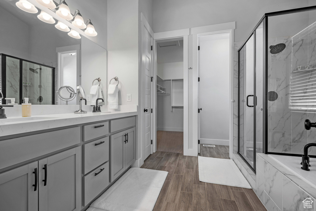 Bathroom with double vanity, wood finished floors, a walk in closet, a sink, and a marble finish shower