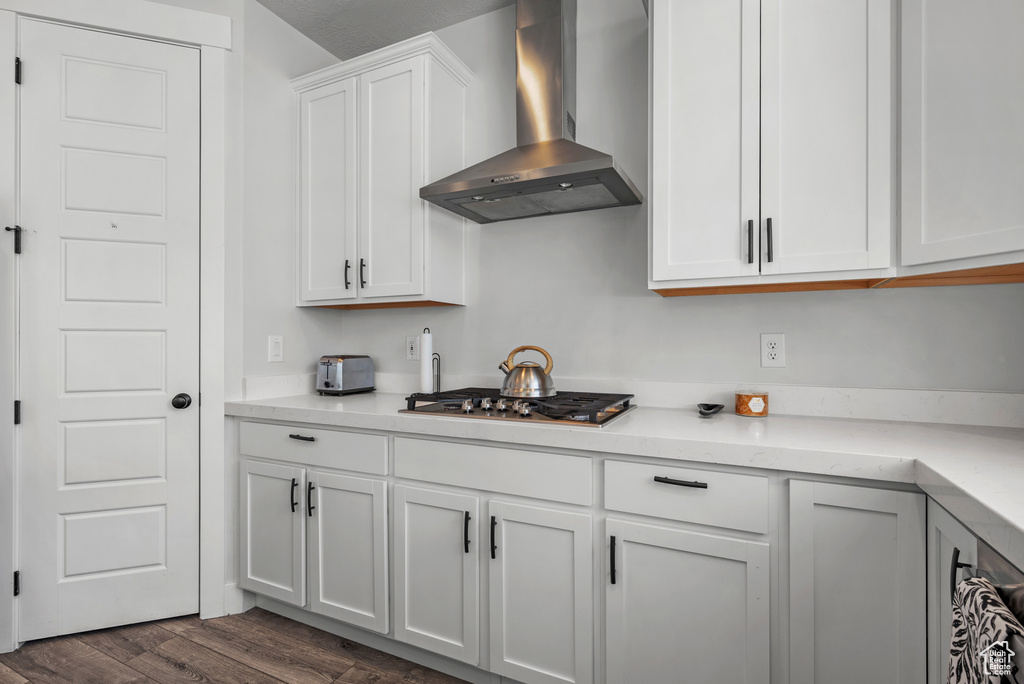 Kitchen featuring dark wood-type flooring, wall chimney exhaust hood, stainless steel gas cooktop, and white cabinetry