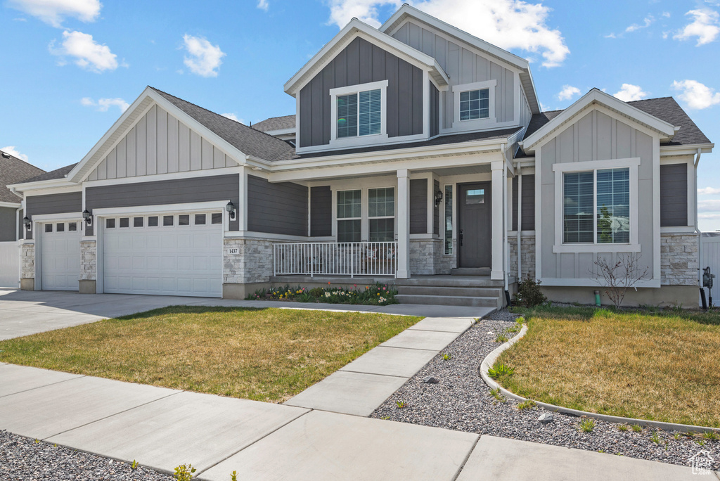 Craftsman-style house featuring a garage, a front lawn, stone siding, board and batten siding, and a porch