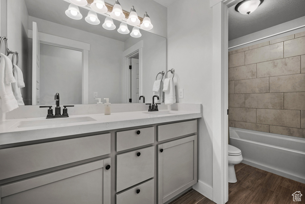 Full bathroom with double vanity, toilet, a sink, and wood finished floors