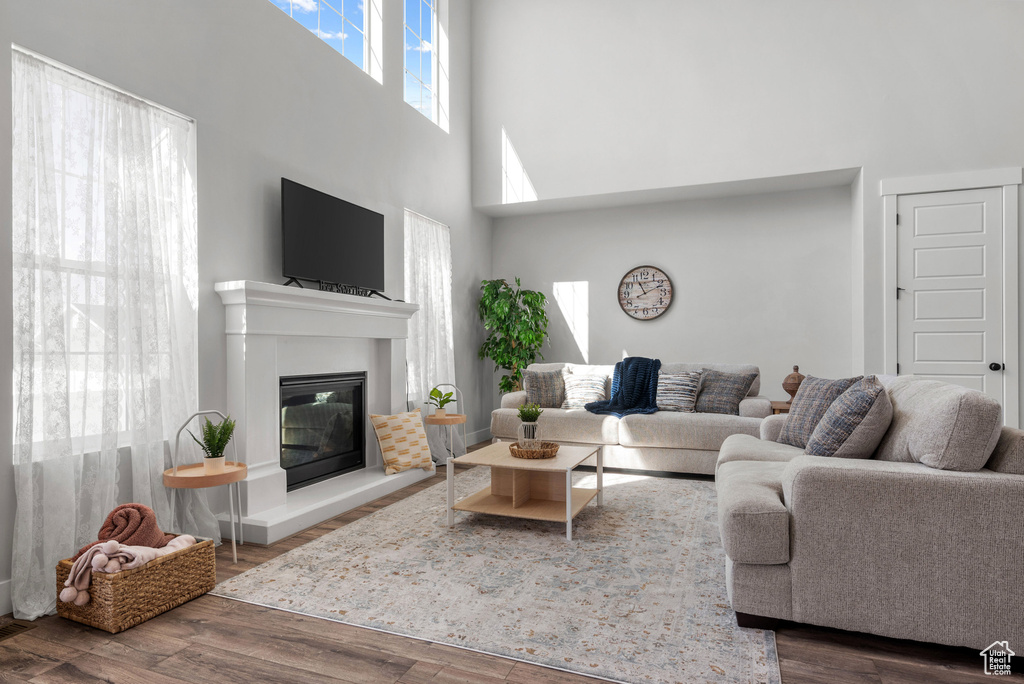 Living room with a glass covered fireplace, wood finished floors, and a towering ceiling