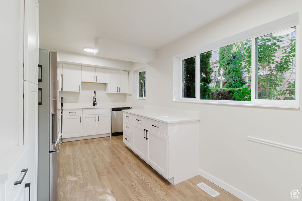 Kitchen with a sink, white cabinets, stainless steel dishwasher, visible vents, and light wood-style floors