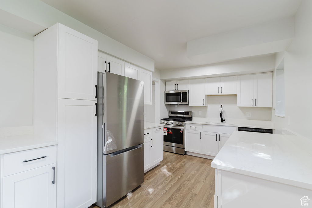 Kitchen with a sink, white cabinetry, light wood-style floors, light countertops, and appliances with stainless steel finishes