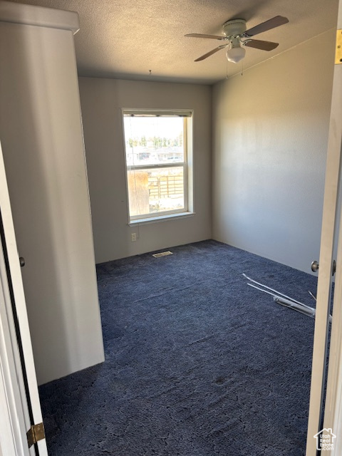 Carpeted empty room featuring a ceiling fan and a textured ceiling