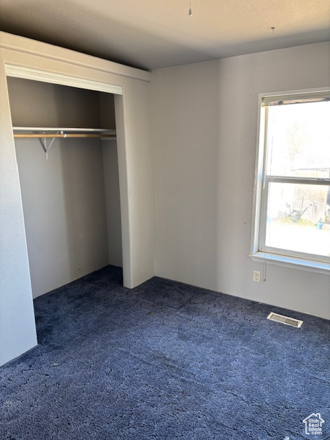 Unfurnished bedroom featuring a closet, dark carpet, and visible vents