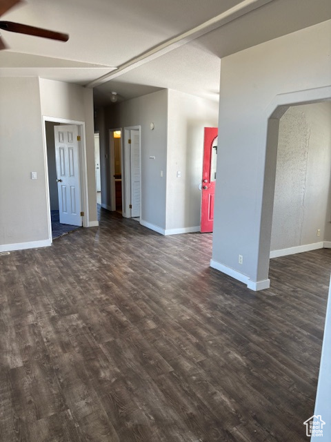 Unfurnished living room with baseboards, arched walkways, ceiling fan, and dark wood-style floors