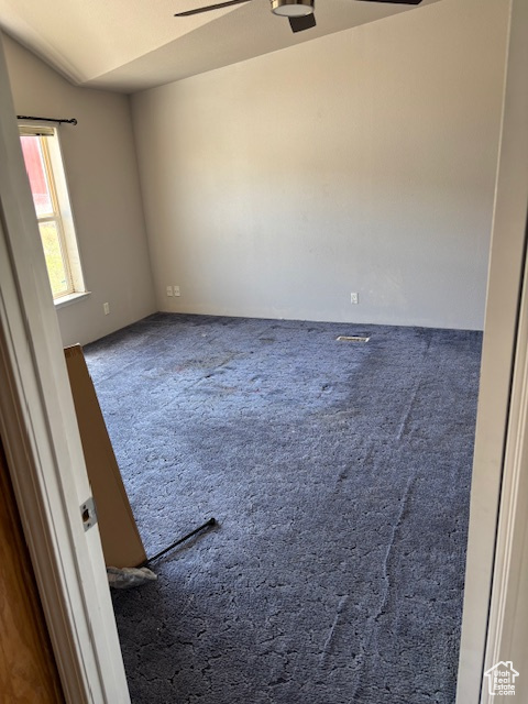 Carpeted empty room featuring a ceiling fan and lofted ceiling