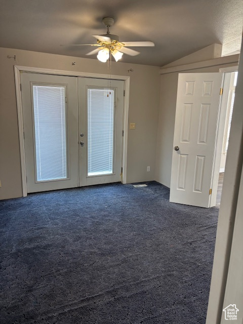Empty room with a ceiling fan, vaulted ceiling, french doors, and dark carpet
