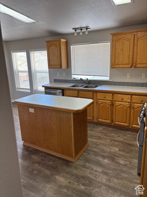 Kitchen with a textured ceiling, stainless steel dishwasher, a sink, light countertops, and dark wood-type flooring