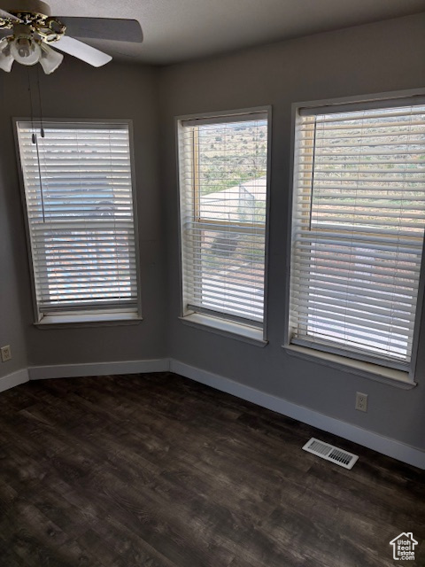 Empty room featuring visible vents, dark wood-style flooring, baseboards, plenty of natural light, and a ceiling fan