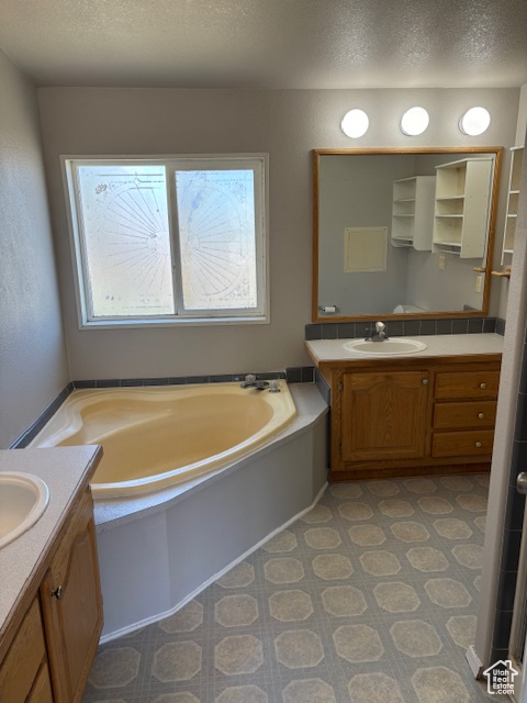 Full bathroom featuring a sink, a textured ceiling, two vanities, and a healthy amount of sunlight