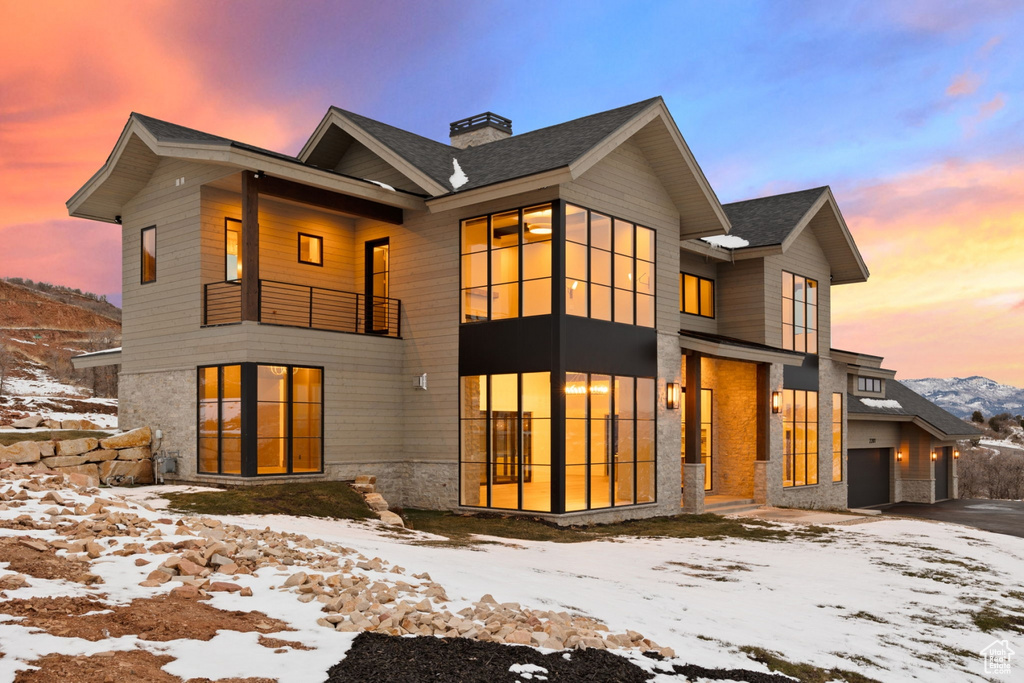 Snow covered back of property with a garage, a chimney, and a balcony