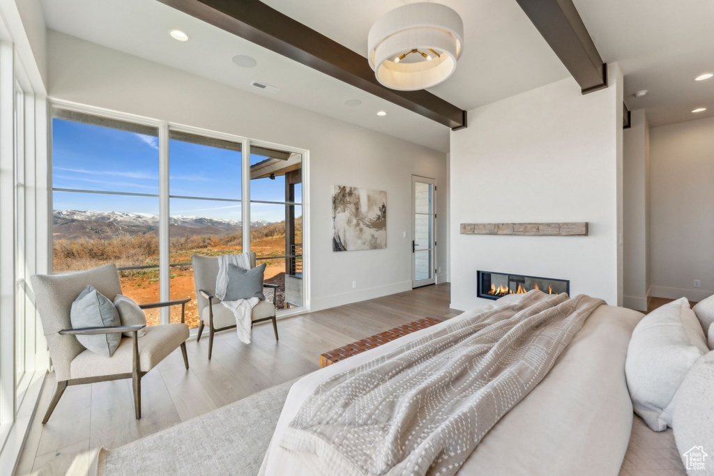Bedroom with recessed lighting, beamed ceiling, a glass covered fireplace, and wood finished floors