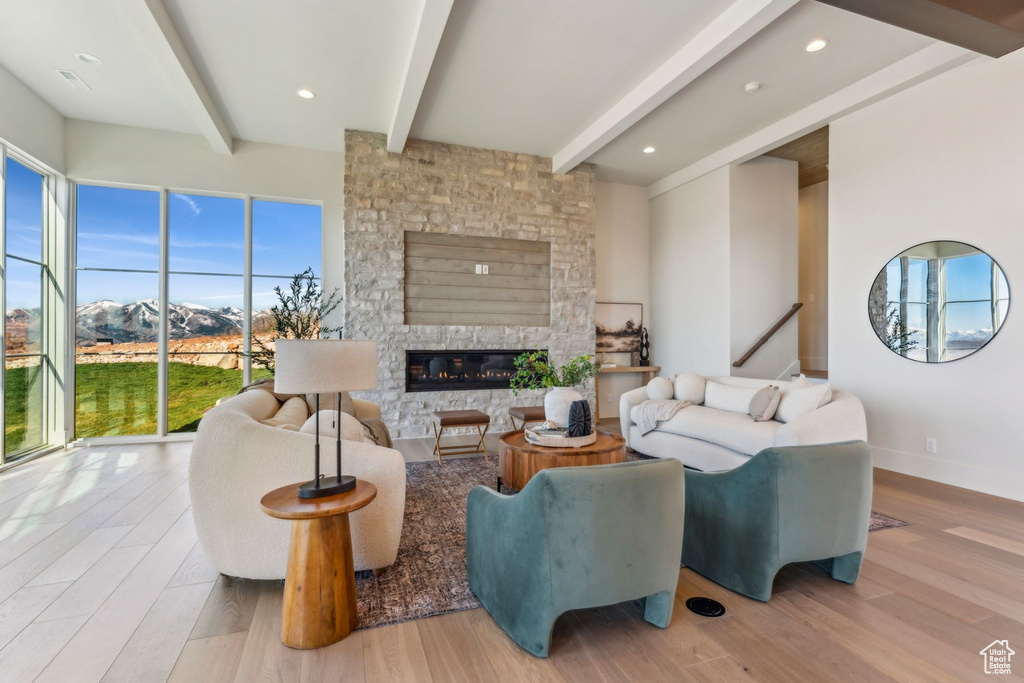 Living area featuring beamed ceiling, a stone fireplace, baseboards, and wood finished floors
