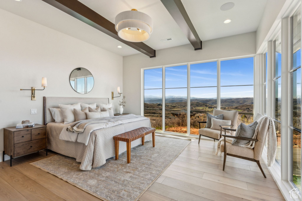 Bedroom with a mountain view, beam ceiling, visible vents, and light wood-style floors