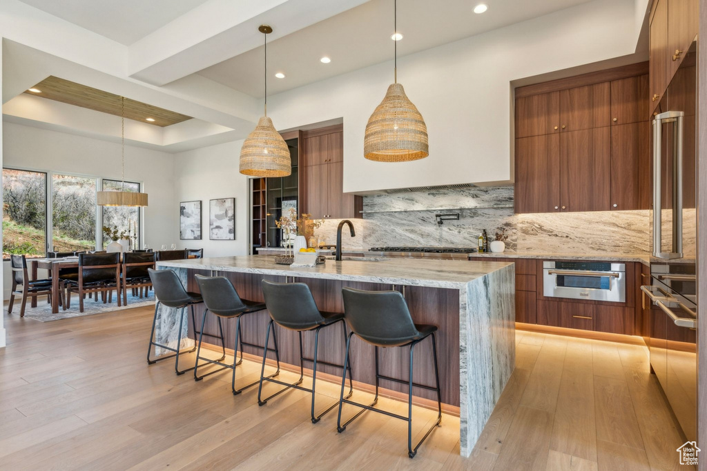 Kitchen featuring brown cabinetry, modern cabinets, a sink, a kitchen breakfast bar, and tasteful backsplash