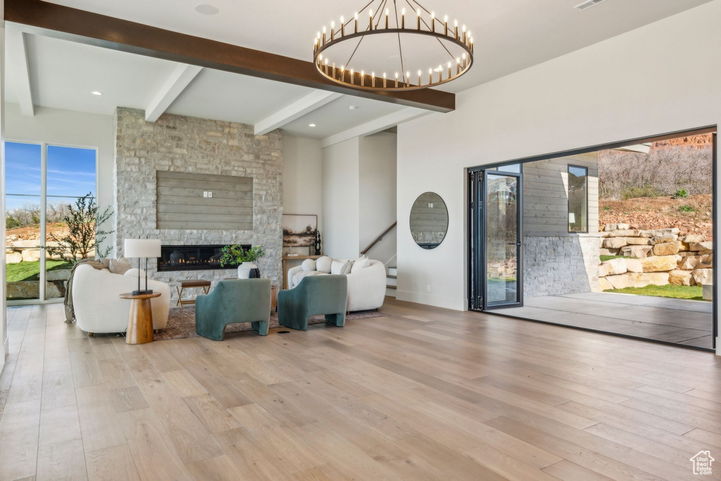 Living room featuring beamed ceiling, a notable chandelier, a fireplace, and wood finished floors