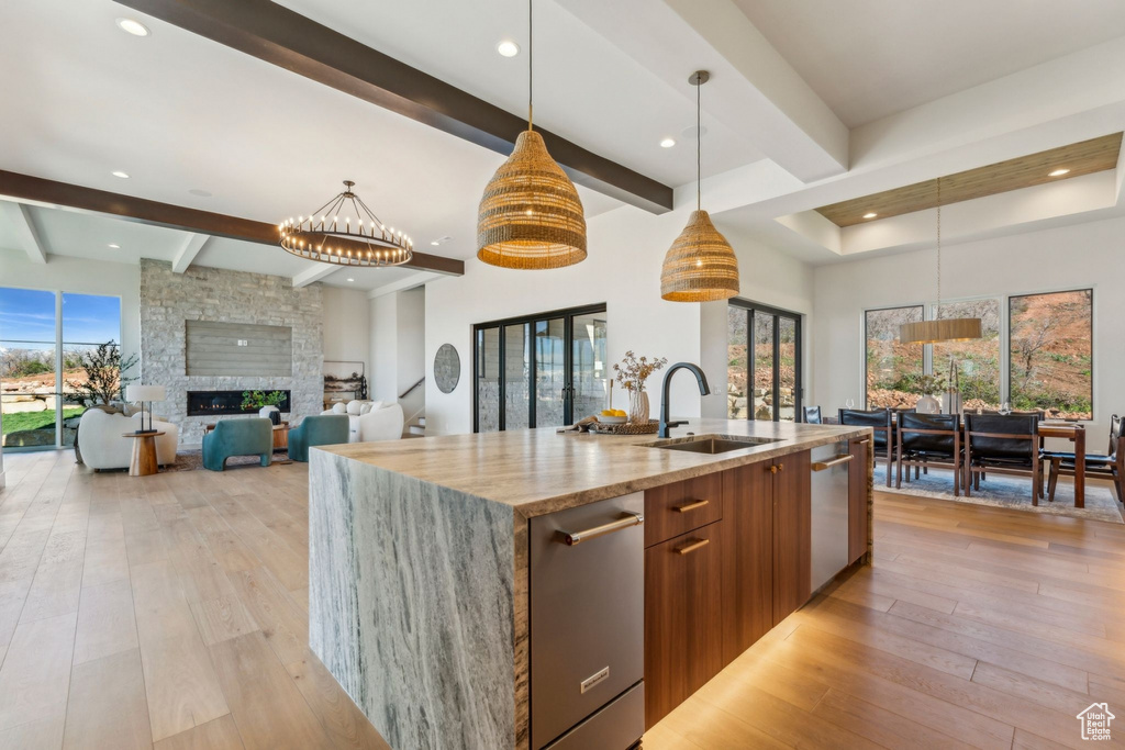 Kitchen featuring a sink, brown cabinets, an island with sink, light stone countertops, and modern cabinets