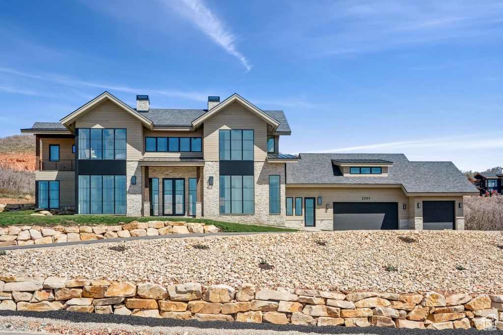 View of front of house with a shingled roof, a chimney, a garage, and stone siding