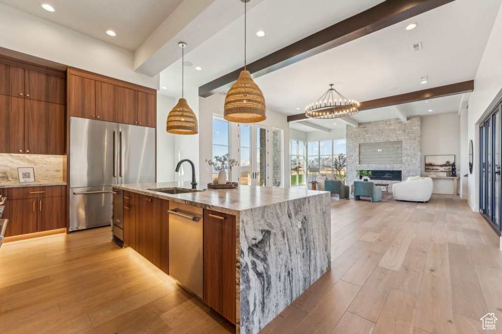 Kitchen featuring modern cabinets, a sink, brown cabinets, beamed ceiling, and appliances with stainless steel finishes