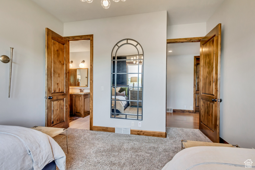 Bedroom with an inviting chandelier, ensuite bathroom, wood finished floors, and visible vents