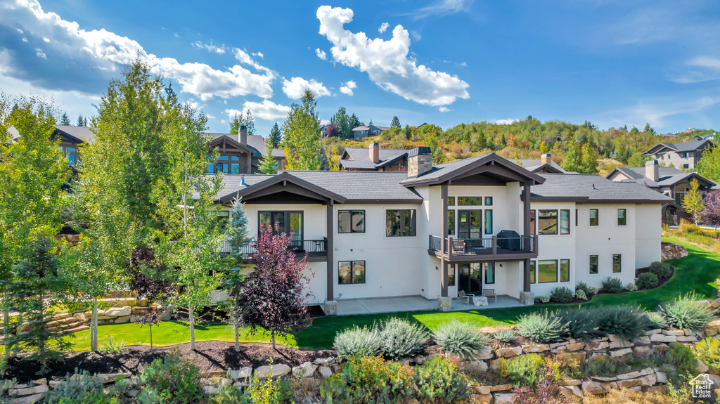Back of house with a lawn, stucco siding, a patio area, and a balcony