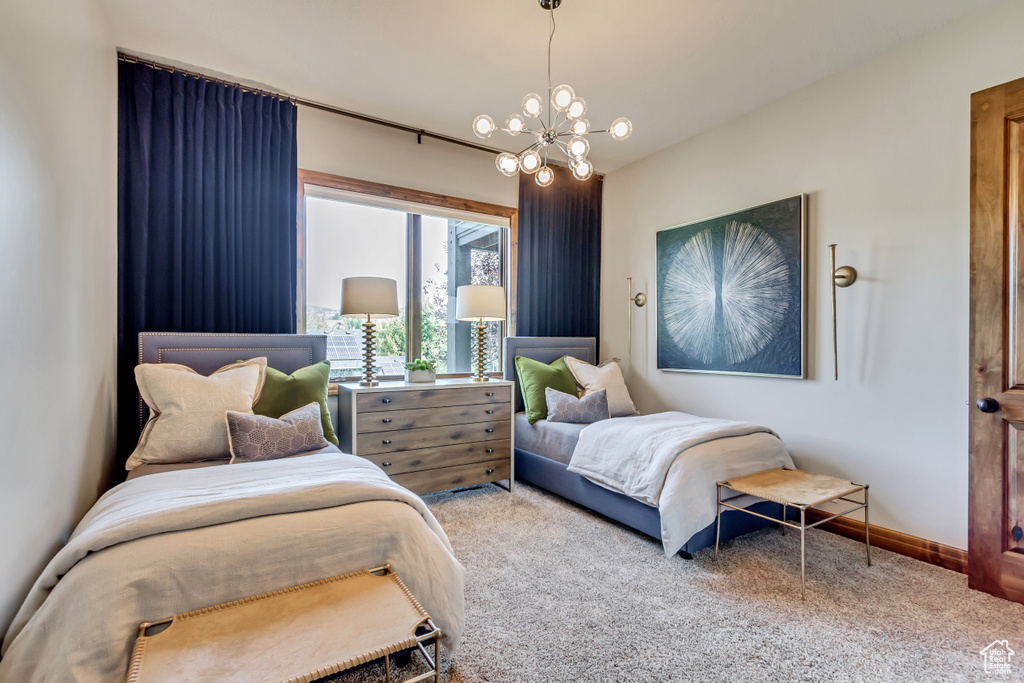 Carpeted bedroom featuring baseboards and a notable chandelier