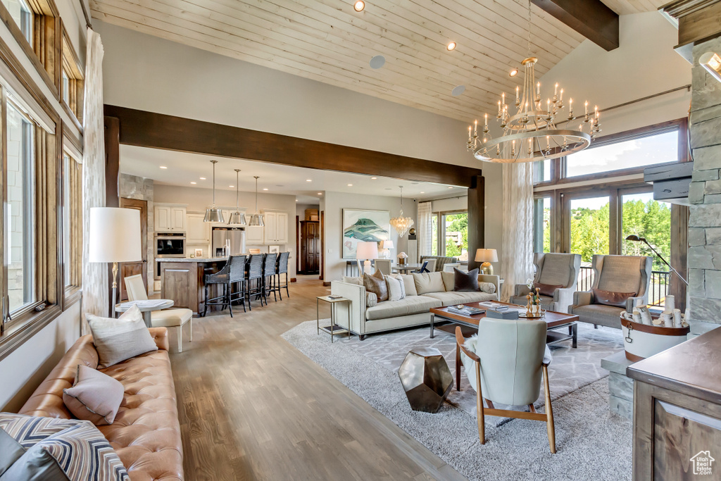 Living area with a high ceiling, an inviting chandelier, beam ceiling, light wood-style floors, and wooden ceiling