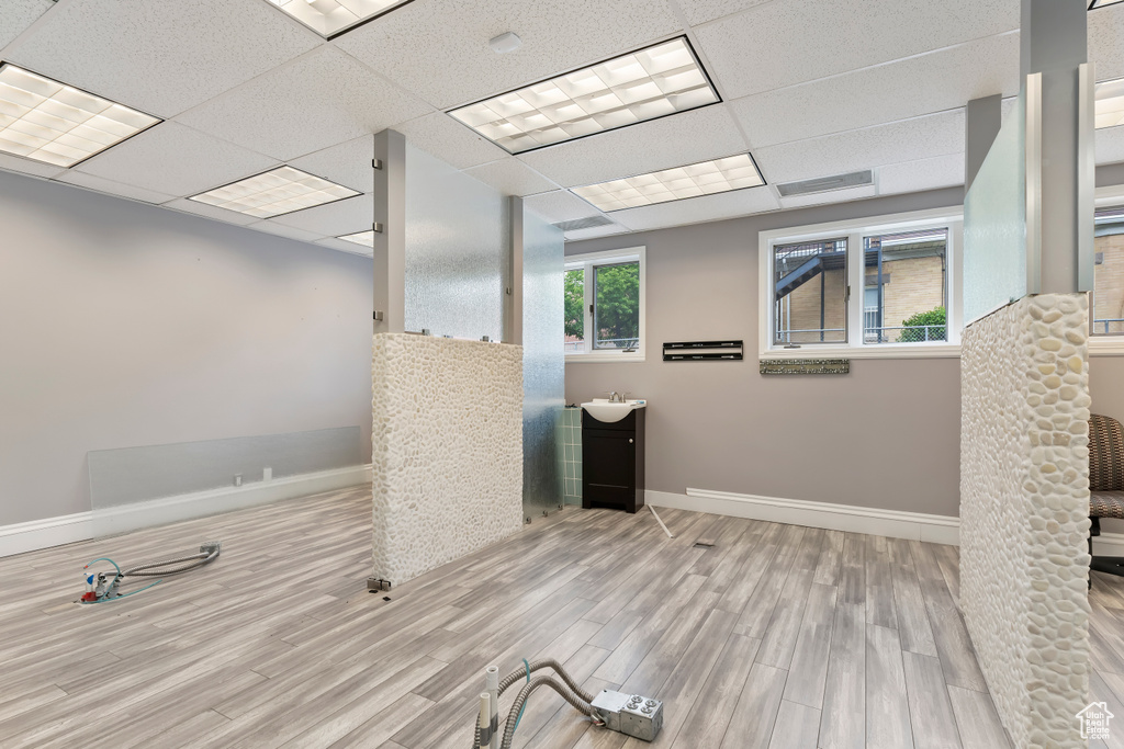 Basement featuring baseboards, a drop ceiling, a sink, and wood finished floors