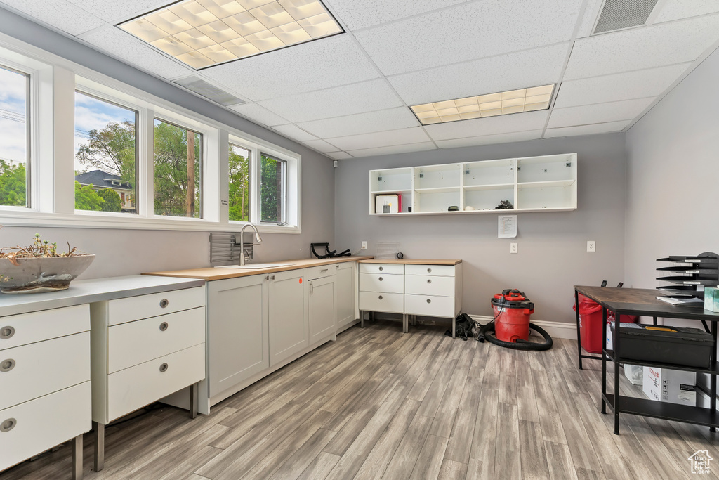 Kitchen featuring light wood finished floors, a sink, a paneled ceiling, white cabinets, and baseboards