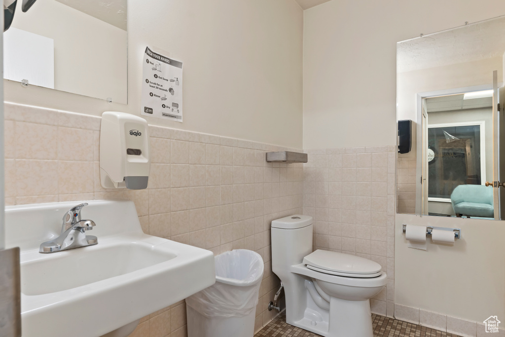 Bathroom featuring toilet, tile walls, tile patterned flooring, and a sink