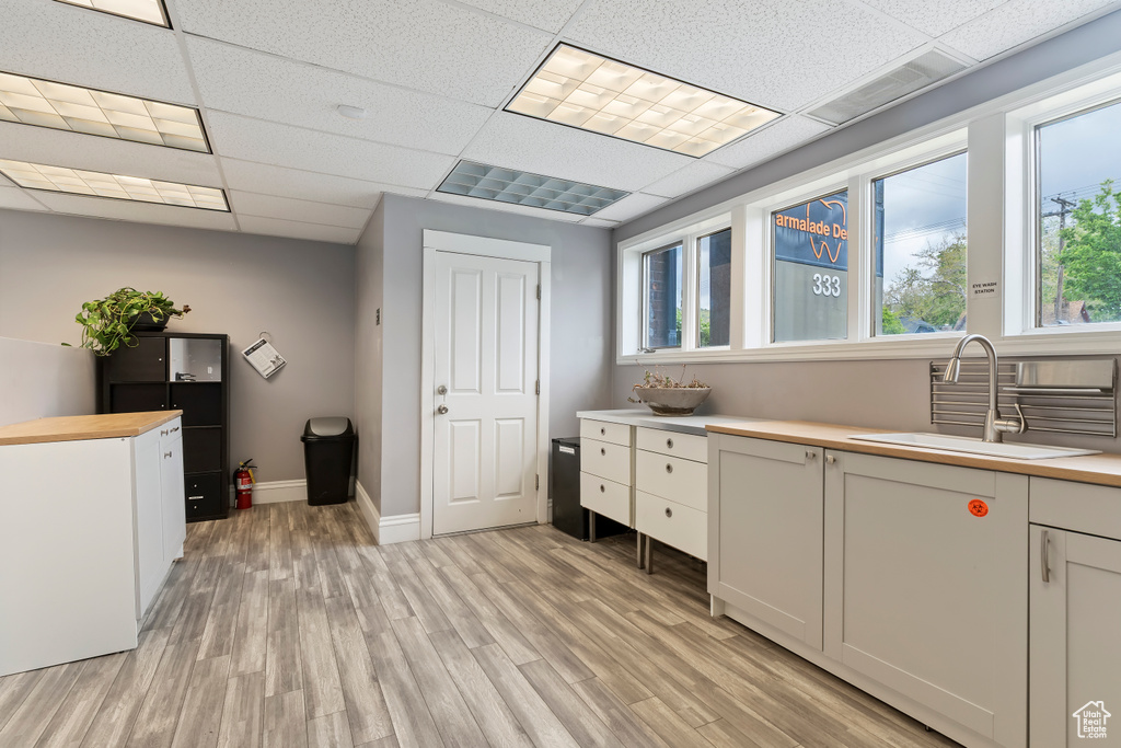 Kitchen featuring light wood-style floors, a drop ceiling, baseboards, and a sink