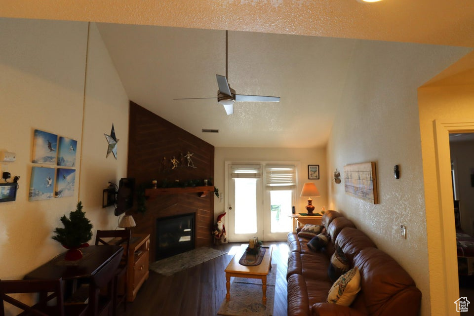Living room featuring lofted ceiling, a ceiling fan, a glass covered fireplace, and wood finished floors
