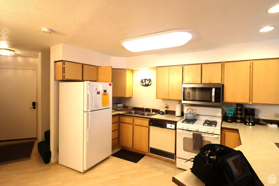 Kitchen with light wood finished floors, a sink, white appliances, light countertops, and recessed lighting