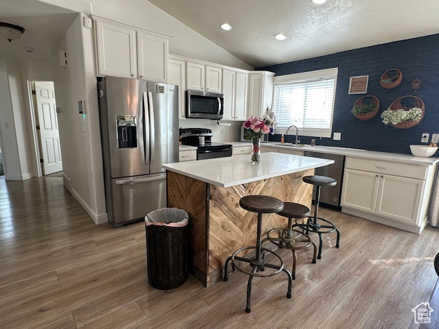 Kitchen featuring stainless steel appliances, white cabinets, a kitchen island, vaulted ceiling, and a sink