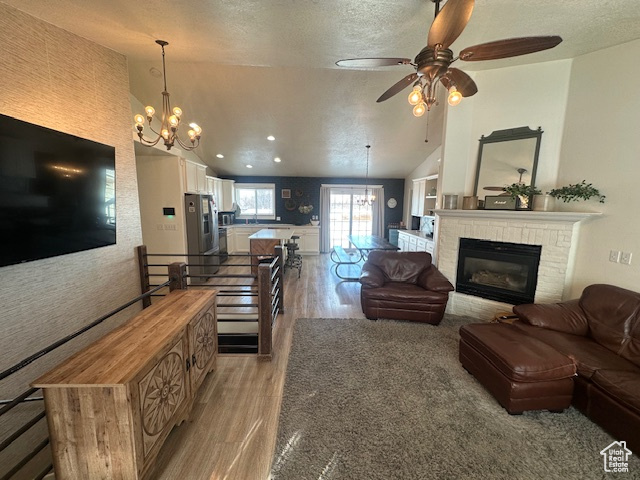 Living area featuring a chandelier, light wood-style flooring, a textured ceiling, a ceiling fan, and lofted ceiling