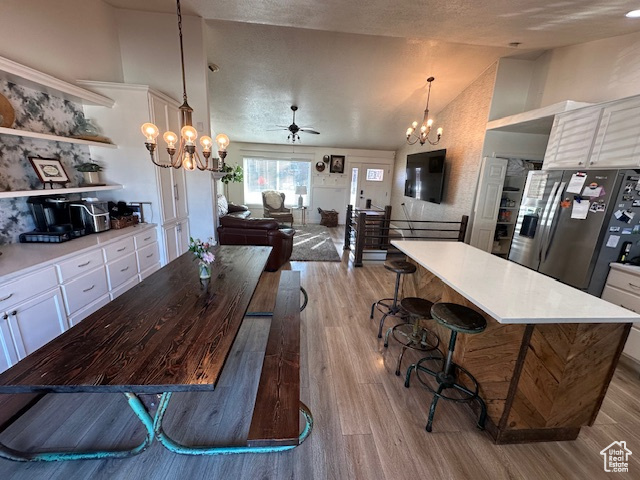 Dining room featuring a chandelier, high vaulted ceiling, ceiling fan, and light wood finished floors