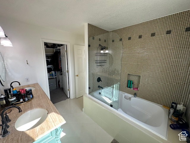 Full bath with tile patterned floors, tiled shower / bath combo, a textured ceiling, a spacious closet, and vanity