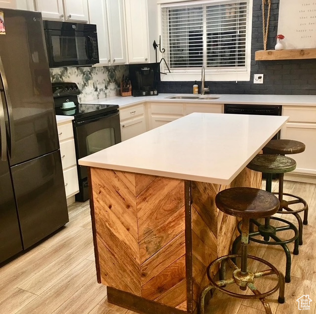 Kitchen with black appliances, light wood-style floors, a sink, a kitchen breakfast bar, and light countertops