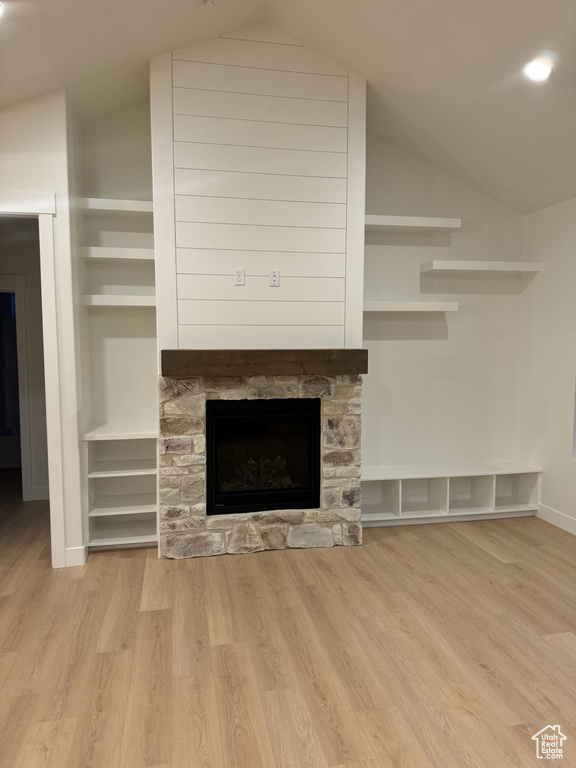 Unfurnished living room with lofted ceiling, baseboards, a stone fireplace, and wood finished floors