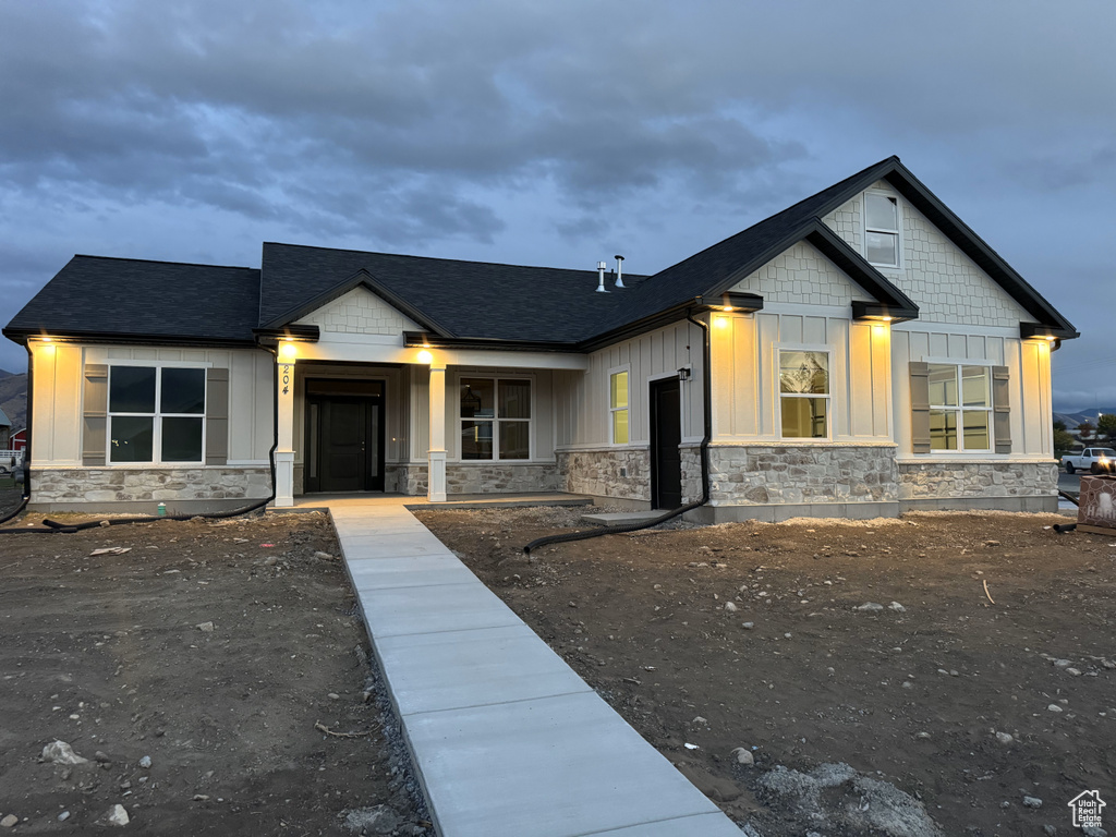 View of front of property with a porch, roof with shingles, stone siding, and board and batten siding