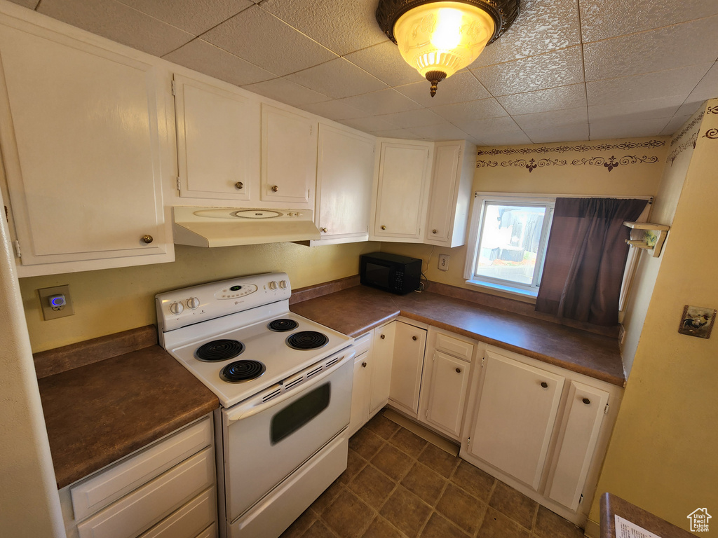 Kitchen with black microwave, electric stove, under cabinet range hood, and dark countertops