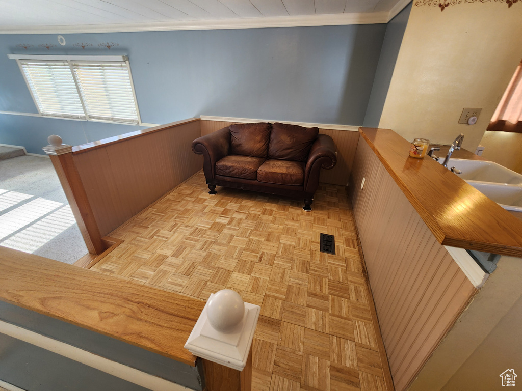 Living area with visible vents, wood walls, crown molding, a wainscoted wall, and an upstairs landing
